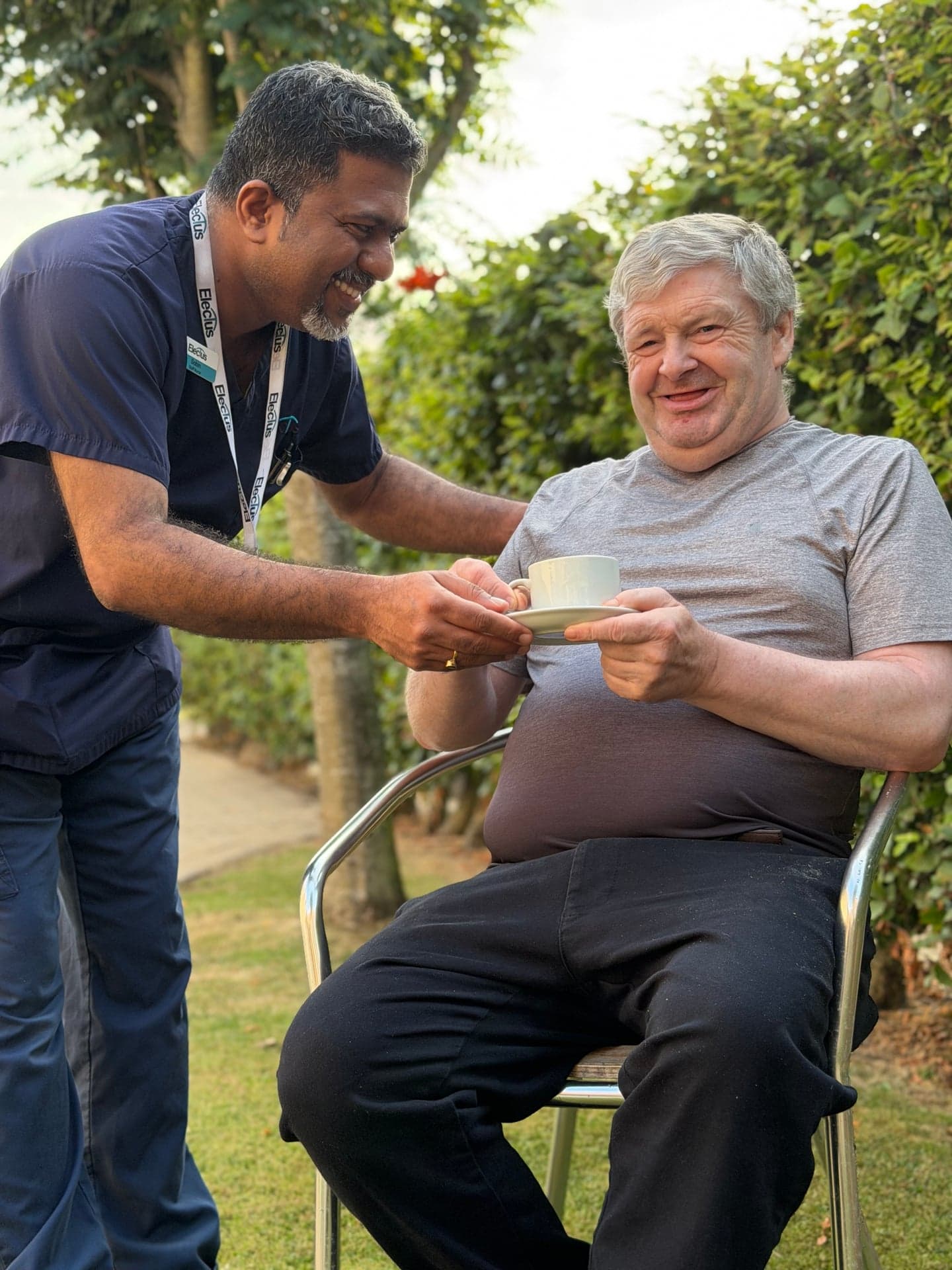 An Electus carer serving tea to a resident in a garden